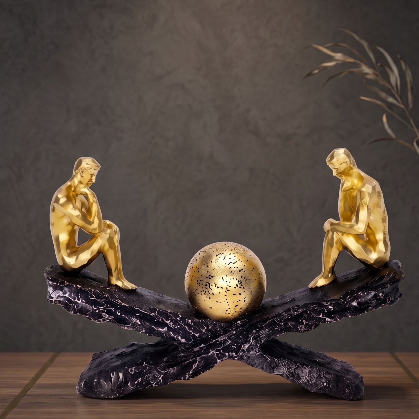Two golden male thinker figures sitting on opposite ends of a textured black crossed base with a textured gold sphere in the center.