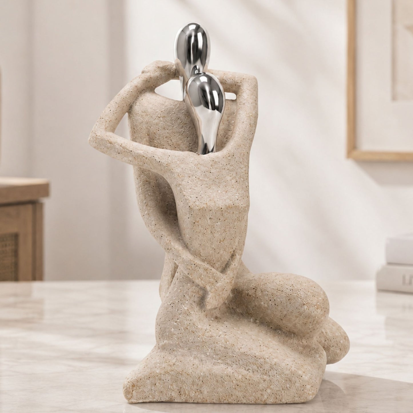 Abstract sculpture of a couple embracing with beige sandstone textured bodies and smooth chrome silver heads.