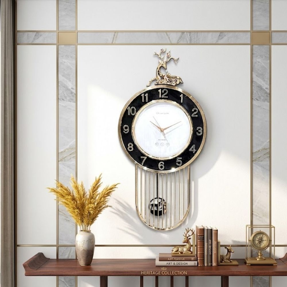 Contemporary round wall clock with a black outer ring, white dial face, topped with a sitting golden stag sculpture and framed by a gold wire cage pendulum below.
