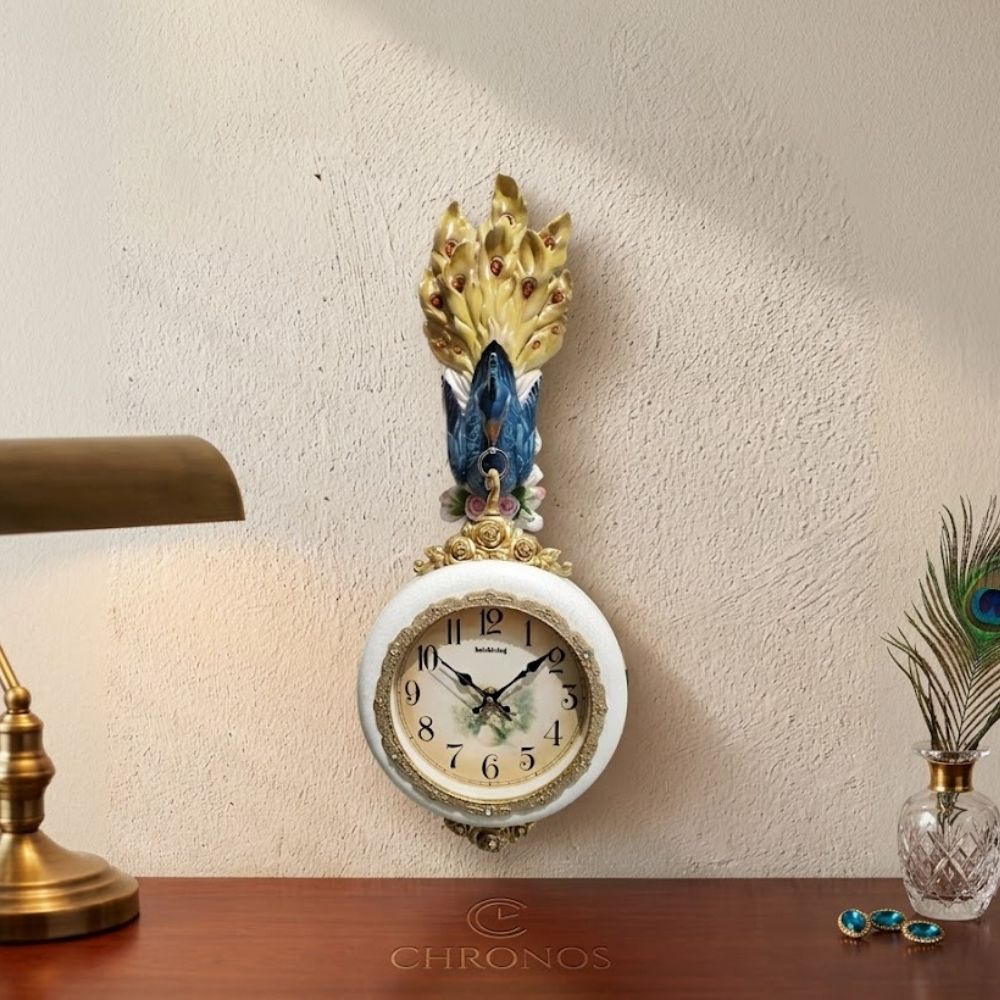 Decorative round white wall clock featuring an ornate blue peacock with flared golden feathers mounted on top, detailed with floral accents and a beige vintage dial.