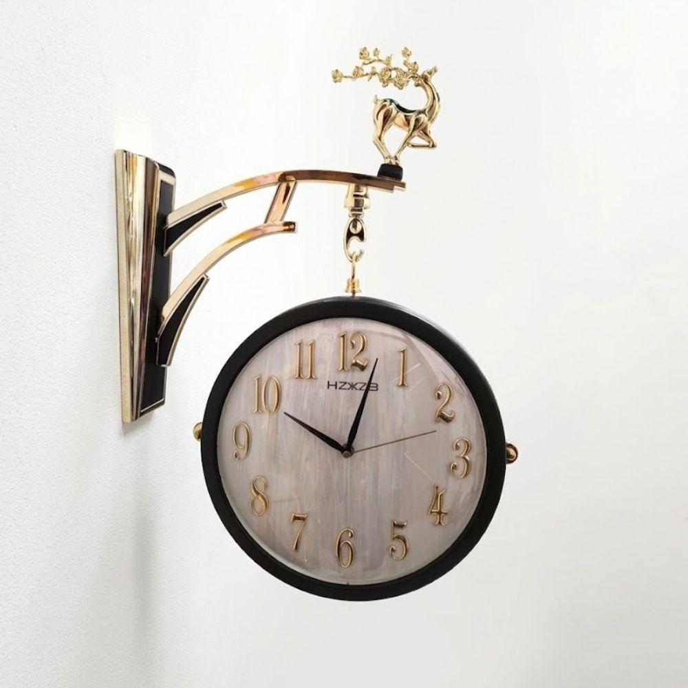 Double-sided hanging station wall clock featuring a matte black frame, brushed marble-textured dial, and raised gold numbers, suspended from a polished gold and black wall bracket topped with a standing golden stag figurine.