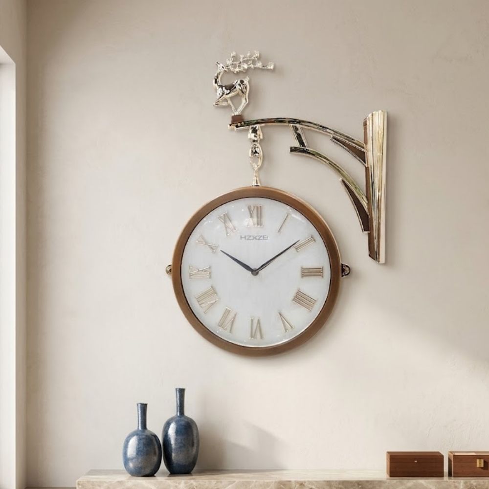 Double-sided hanging station wall clock with a white dial face, bronze-toned rim, and silver Roman numerals, suspended from a polished silver wall bracket topped with a standing deer figurine.