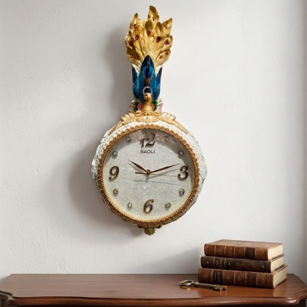 Elegant round white wall clock adorned with a crown of golden peacock feathers, blue avian body, floral accents, and a glittering textured dial with crystal hour indices.