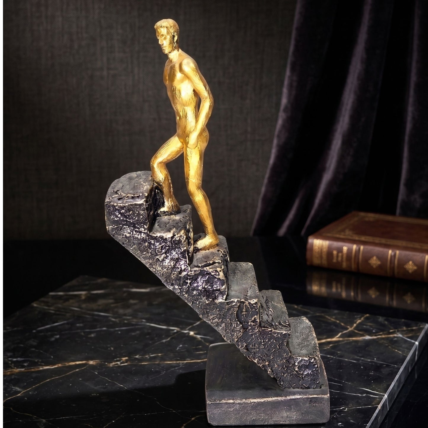 Golden male figure climbing up a black textured stone staircase sculpture for office desk and home decor.