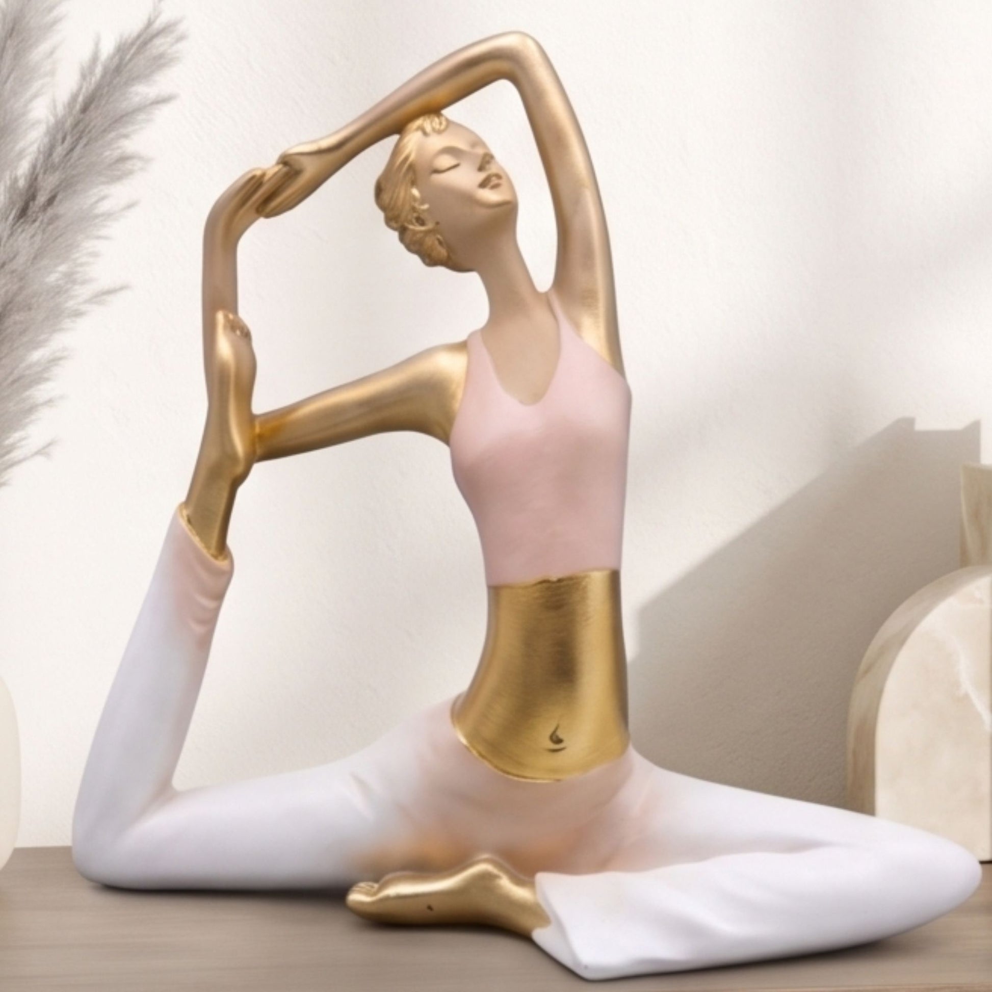 Golden resin sculpture of a woman in a stretching yoga pose wearing a pink top and white pants for home decor.