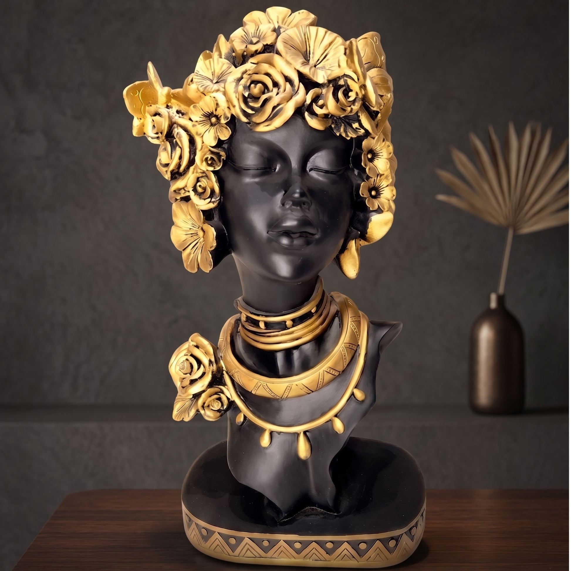 Matte black resin bust sculpture of a serene woman with detailed golden flowers and gold necklace accents.