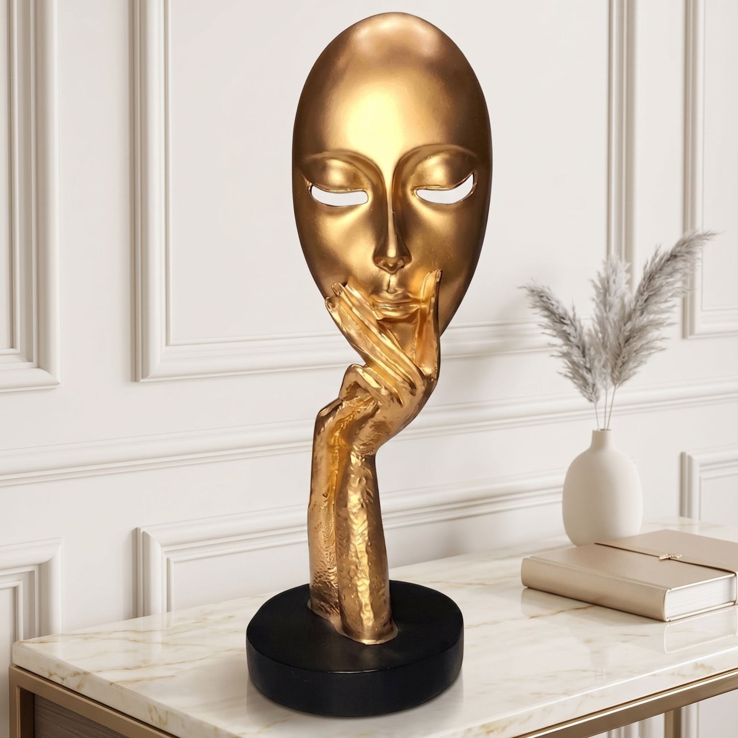 Metallic gold abstract face mask with a hand holding its chin on a black base for tabletop decor.