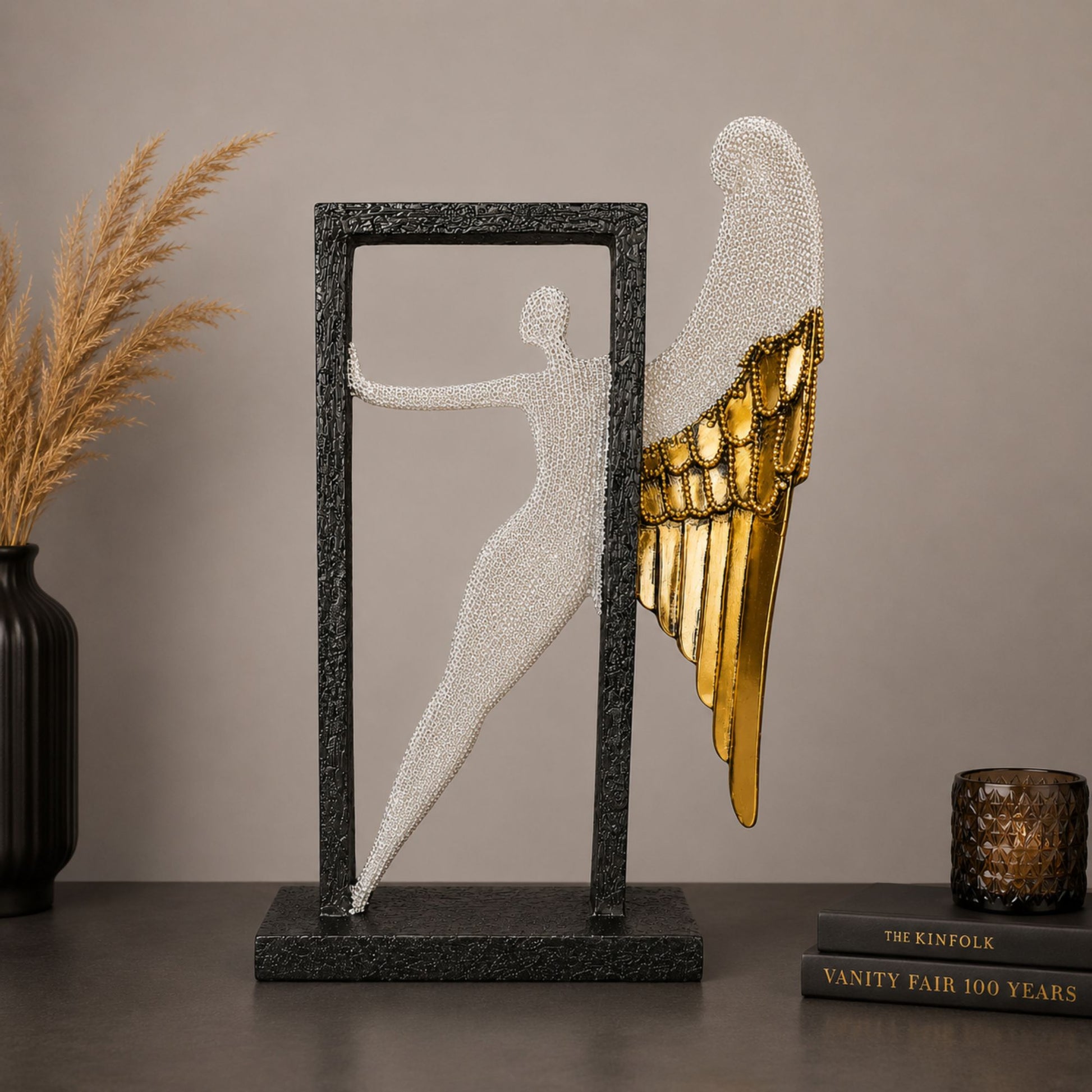 Modern abstract silver textured angel figure with gold wings posing inside a black frame for home table decor.