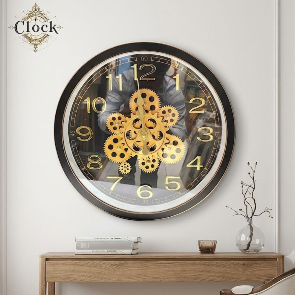 Round black wall clock with a thick black frame, golden numbers, and bright gold gears arranged in a flower pattern at the center.