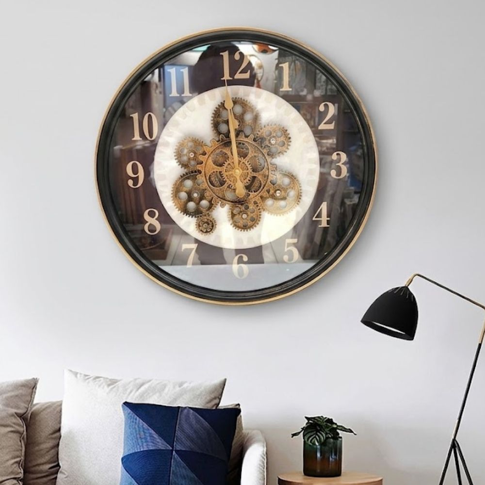 Round black wall clock with white numbers, a gold rim, and exposed antique gold gears arranged in a flower pattern at the center.