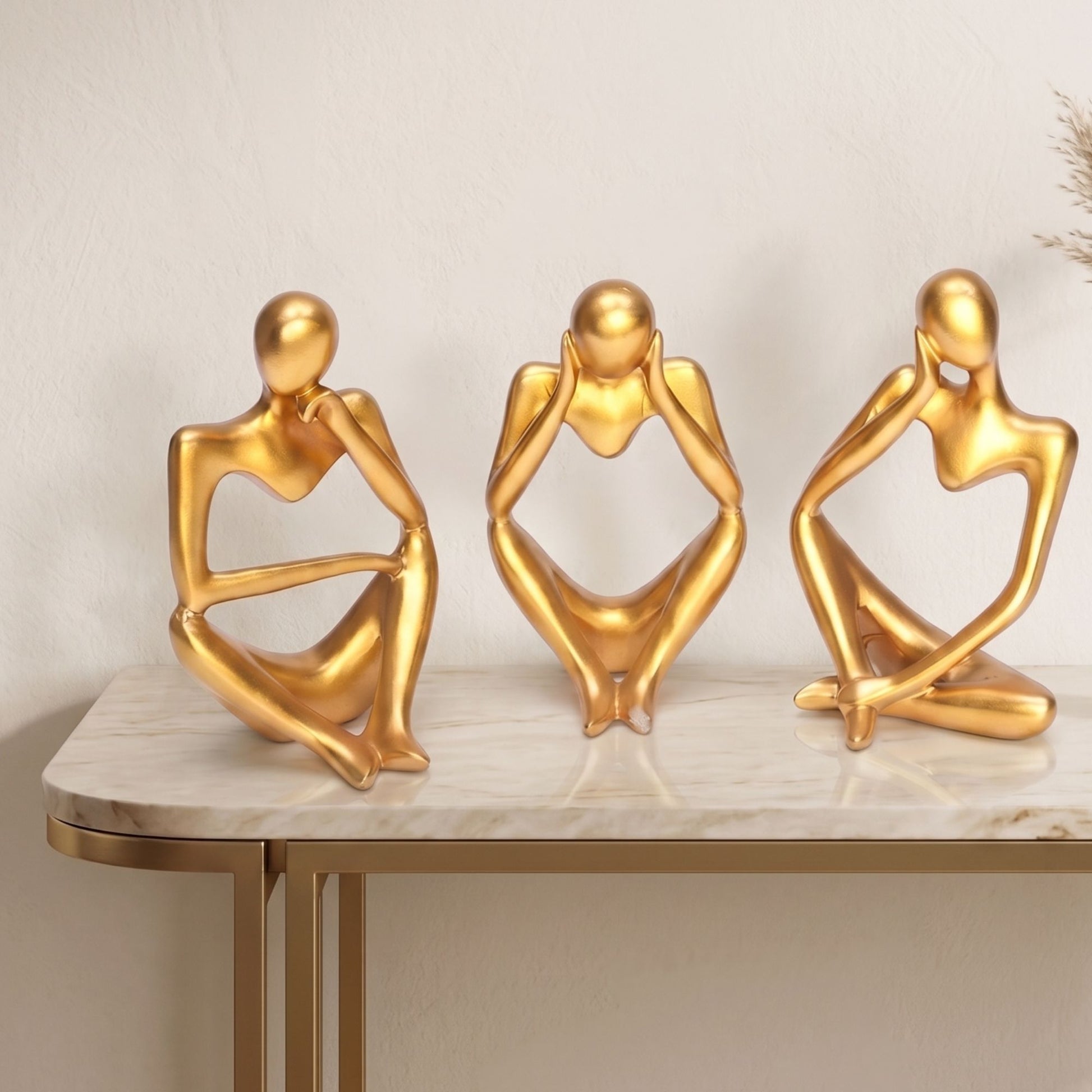 Set of three matte gold abstract thinker statues sitting in different poses on a table for home decor.