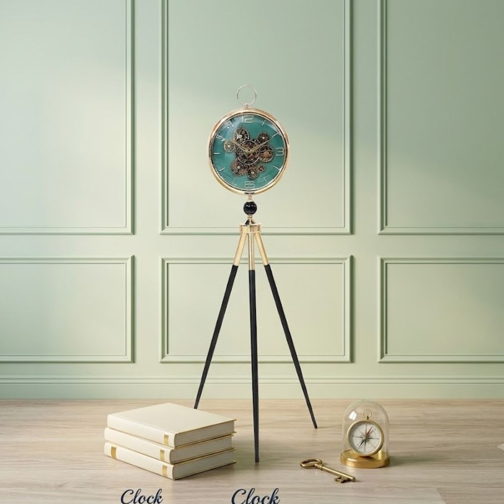 Standing tripod floor clock with black-gold legs and visible gears on a green dial.