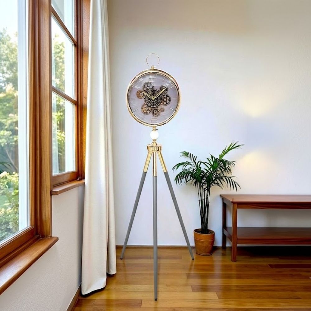 Standing tripod floor clock with grey-gold legs and visible gears on a white dial.