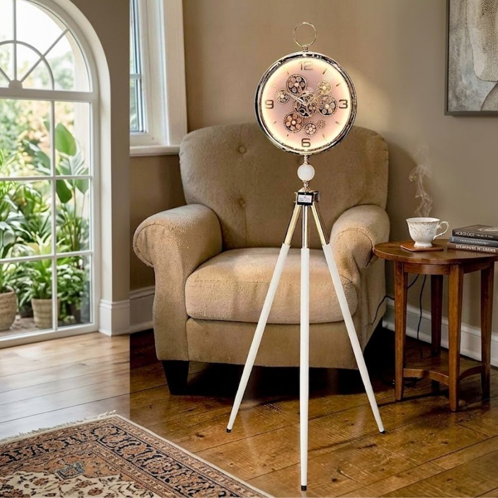 Standing tripod floor clock with white-gold legs and visible gears on a glowing pink dial.